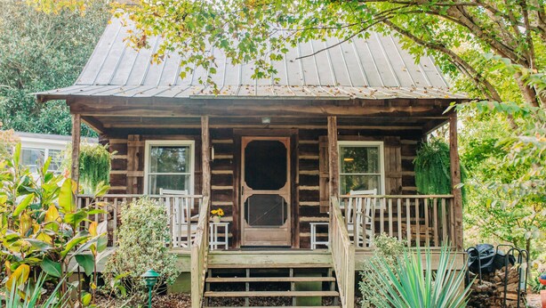 A rustic log cabin with a porch, wooden steps, and a door. - Arrowhead Inn (Durham)