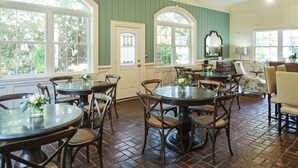 A dining area with round tables and chairs, large windows, and a green wall. - Arrowhead Inn (Durham)