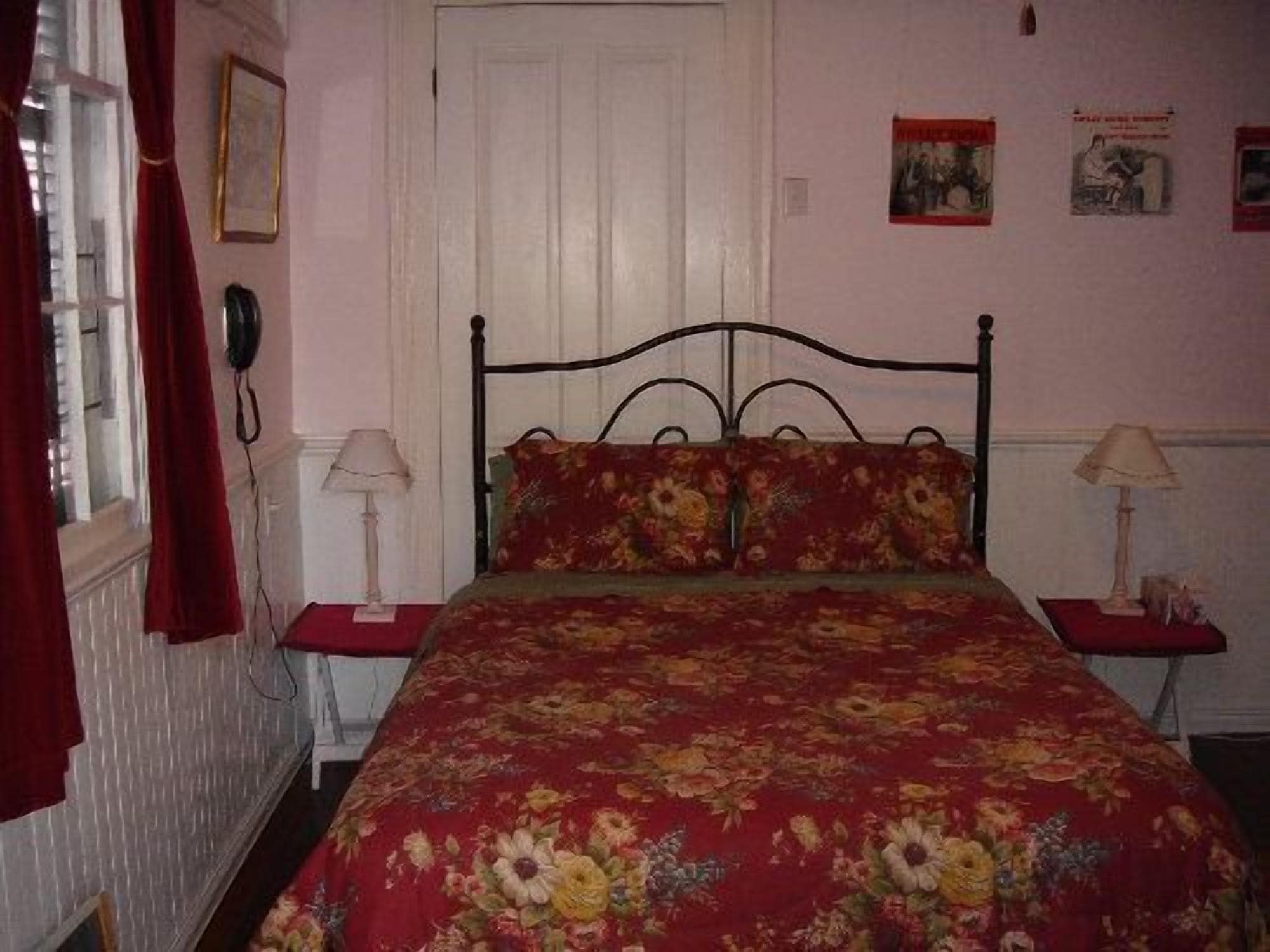 A bedroom with a floral bedspread, a white door, and two bedside tables with lamps.