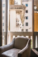 Una habitación con un ventanal grande, una silla y vistas a un edificio con balcones y ventanas.