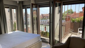 A hotel room with a bed, a chair, and a balcony with a view of a canal and buildings. - Hotel Dei Dragomanni (Venice)