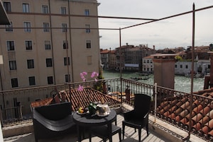 Un balcón con mesa y sillas, con vistas a un canal con edificios y un bote.