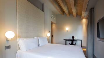 A hotel room with a large bed, bedside lamps, a small table, and a TV mounted on the wall.