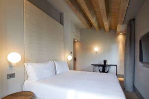 Camera d'albergo con un letto grande, lampade sui comodini, un tavolino e una TV montata a parete.