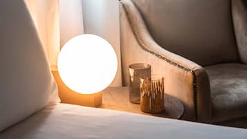 A bed with a bedside lamp, two decorative glass vases, and a leather armchair.