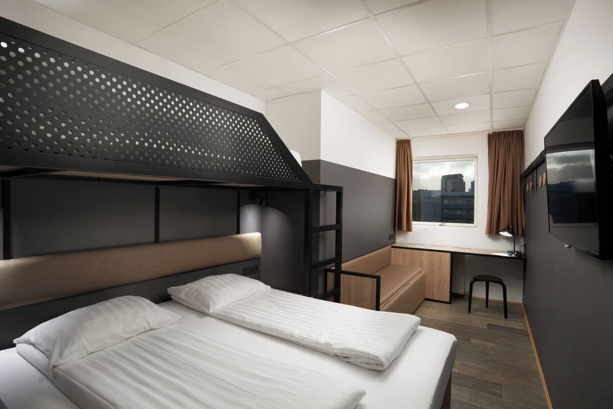 Quarto de hotel compacto com uma cama beliche, uma mesa e uma TV.