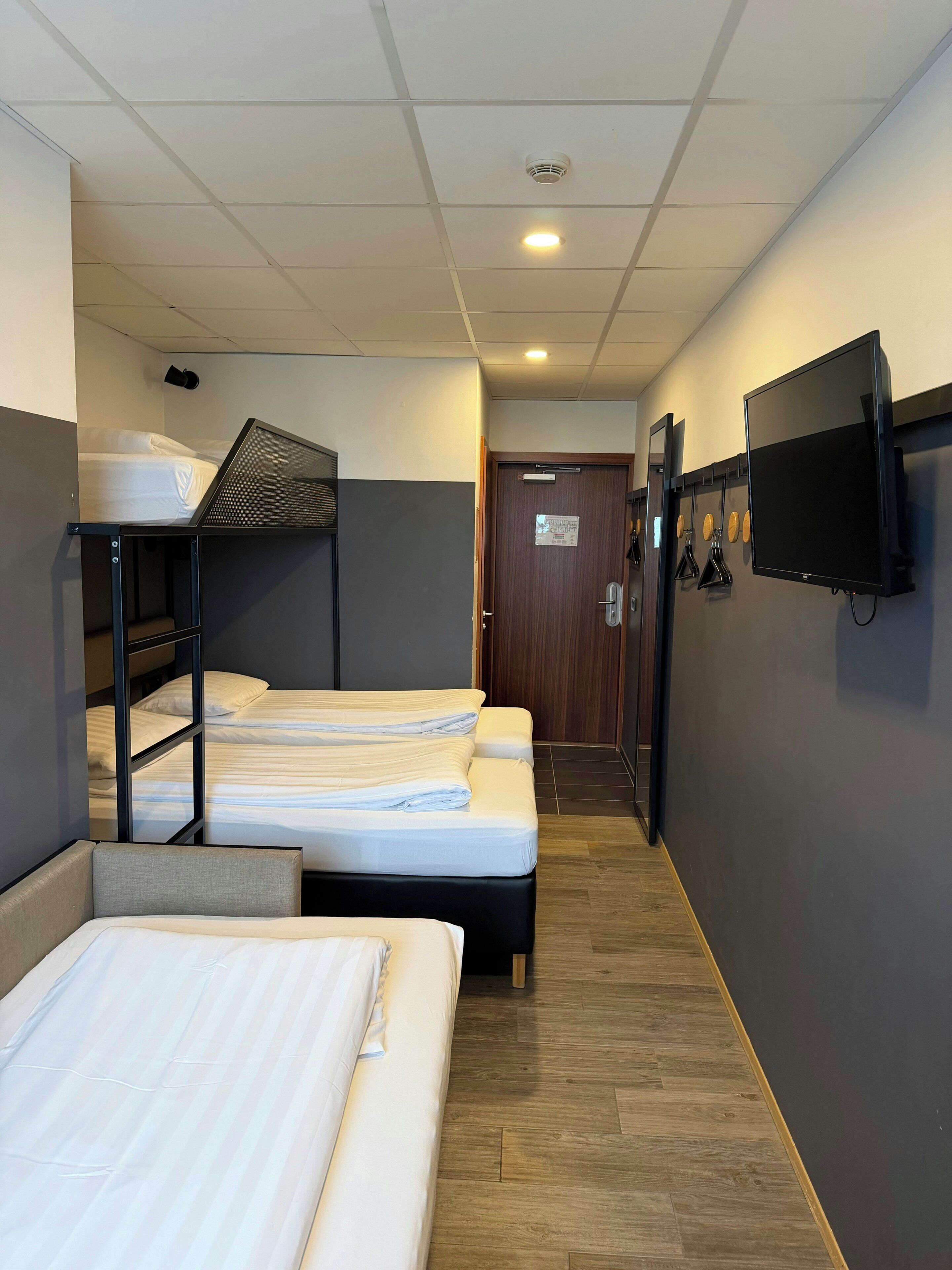 Une chambre d’hôtel avec des lits superposés, un téléviseur fixé au mur et un plancher en bois.
