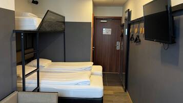 A hotel room with bunk beds, a television mounted on the wall, and a wooden floor.