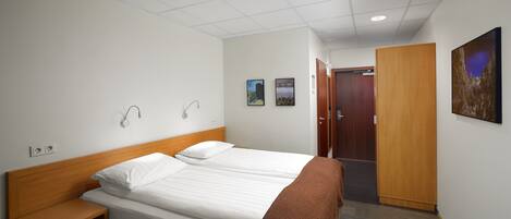 A hotel room with two beds, a wooden headboard, a bedside table, and a brown throw blanket.