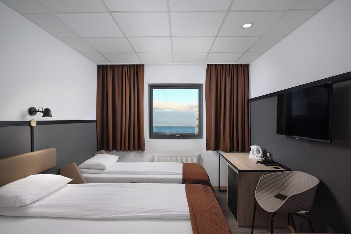 A hotel room with two beds, a desk, a chair, a TV, and a window with curtains.