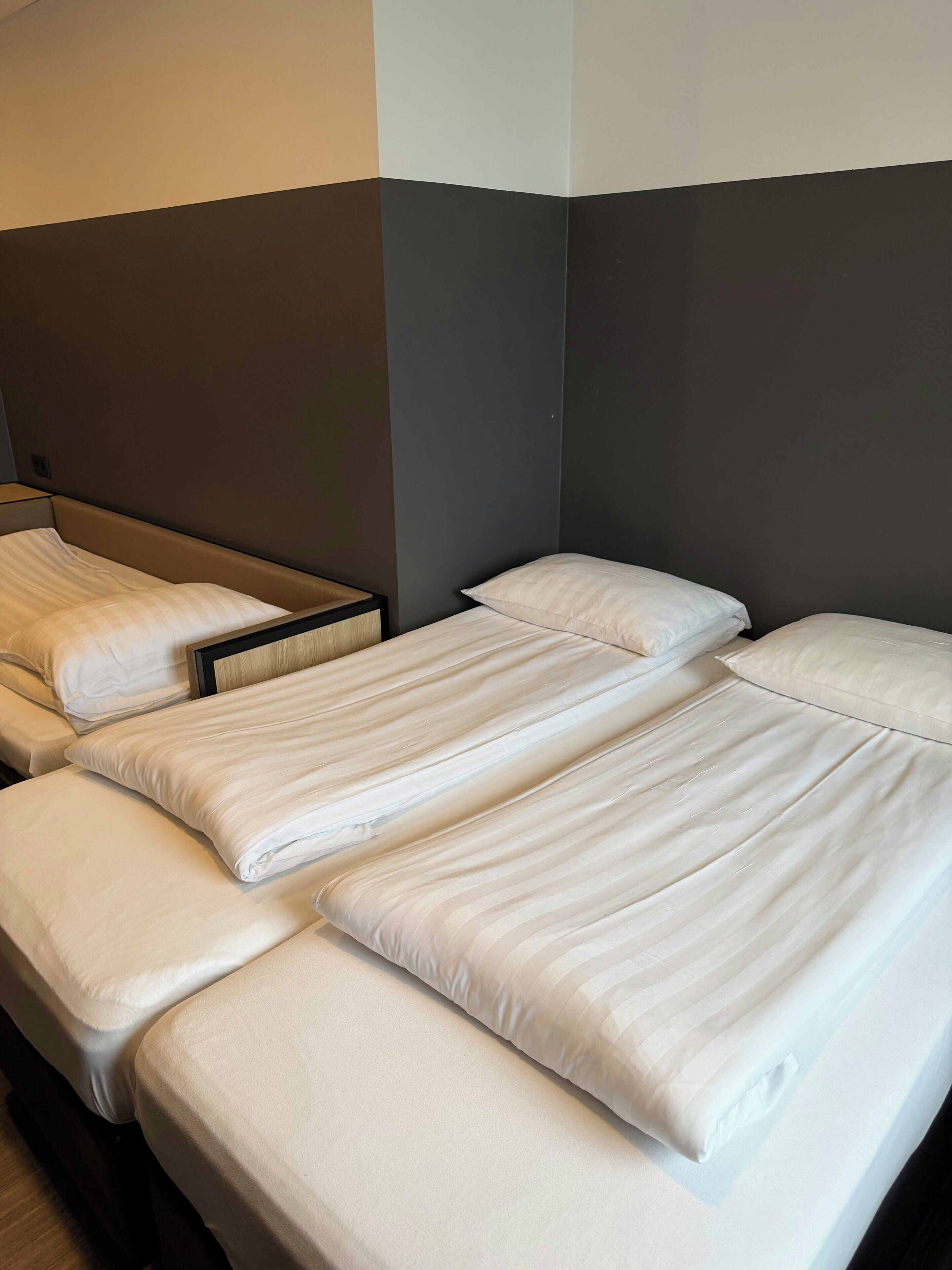 A hotel room with three single beds arranged in a row against a wall with a dark and light color scheme.