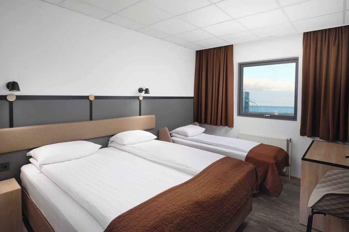 Quarto de hotel com duas camas, uma escrivaninha e uma janela com cortinas.