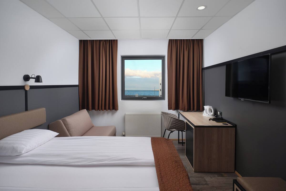 A hotel room with a bed, a desk, a chair, a TV, and a window with curtains.