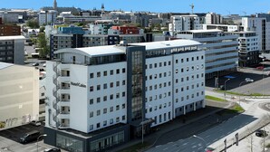A multi-story hotel with a modern design, featuring a prominent 'Hotel Cabin' sign, a parking area, and a street view with surrounding buildings. - Hotel Cabin (Reykjavik)