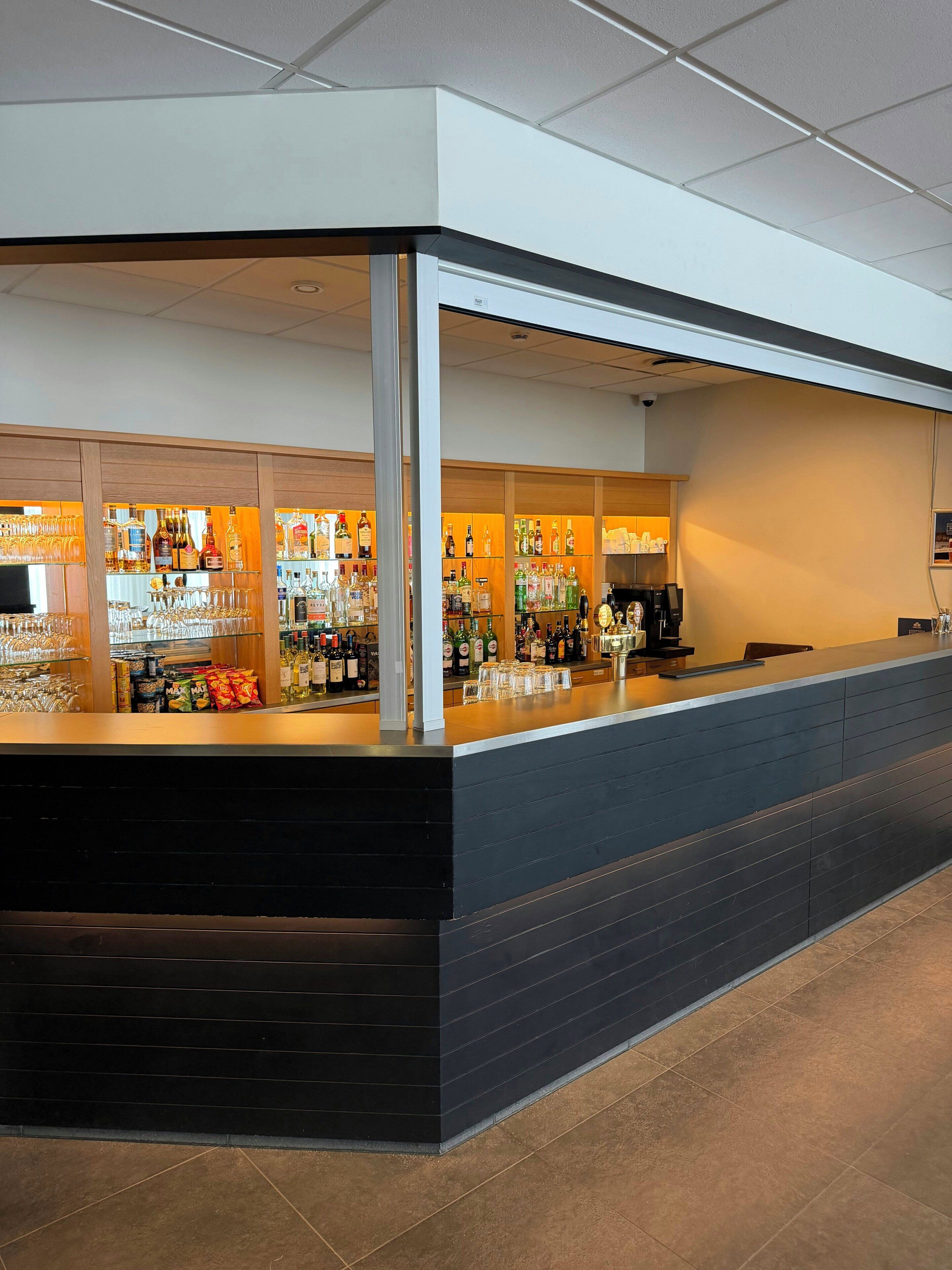 A bar area with a counter, shelves of bottles, glasses, and a coffee machine.