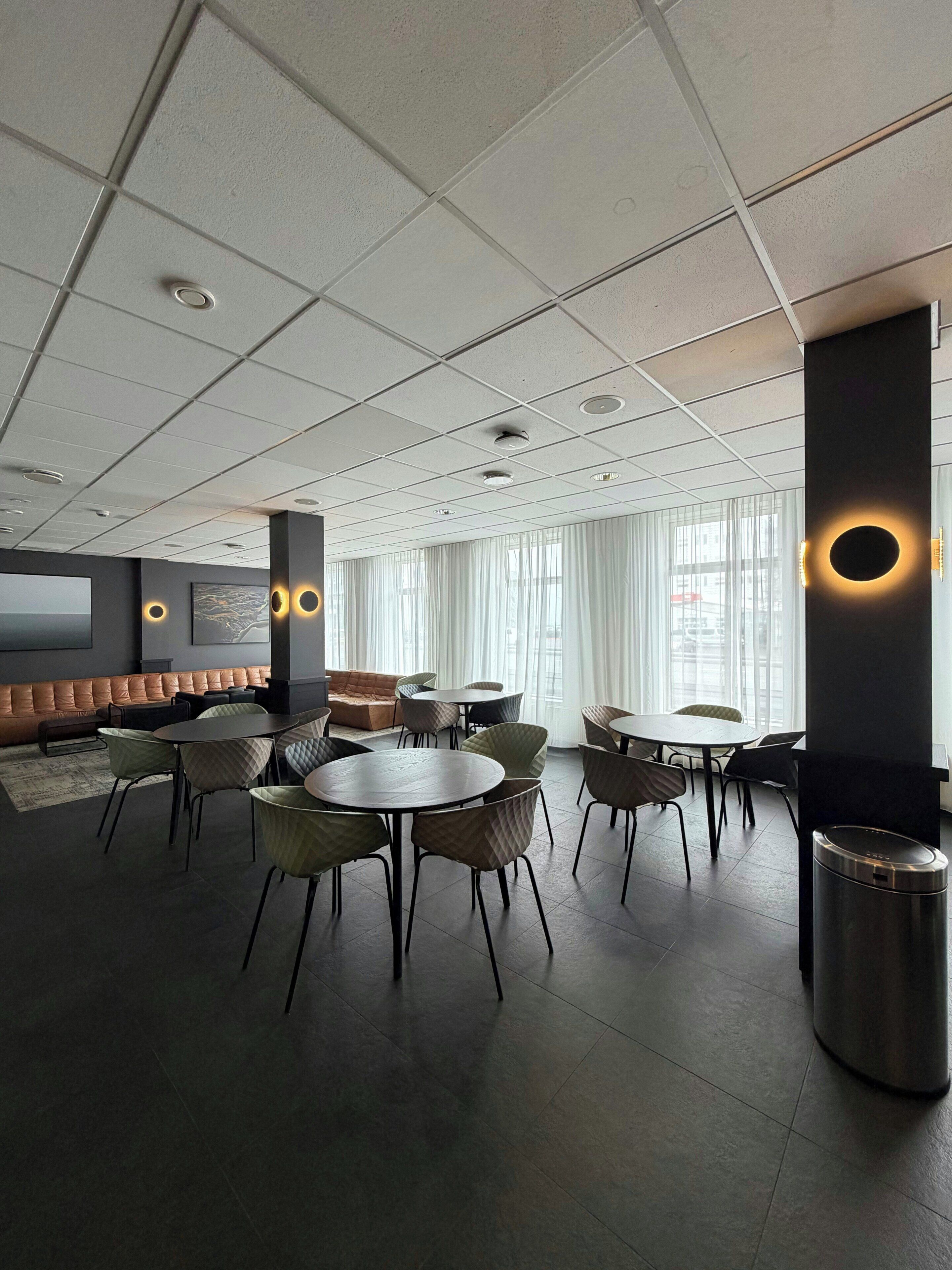 Un espacio lounge moderno con mesas redondas, asientos acolchados y una pantalla grande.