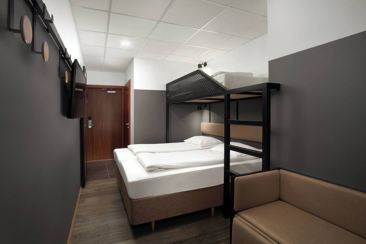 A bunk bed room with a wooden door, a small sofa, and a wall-mounted shelf.