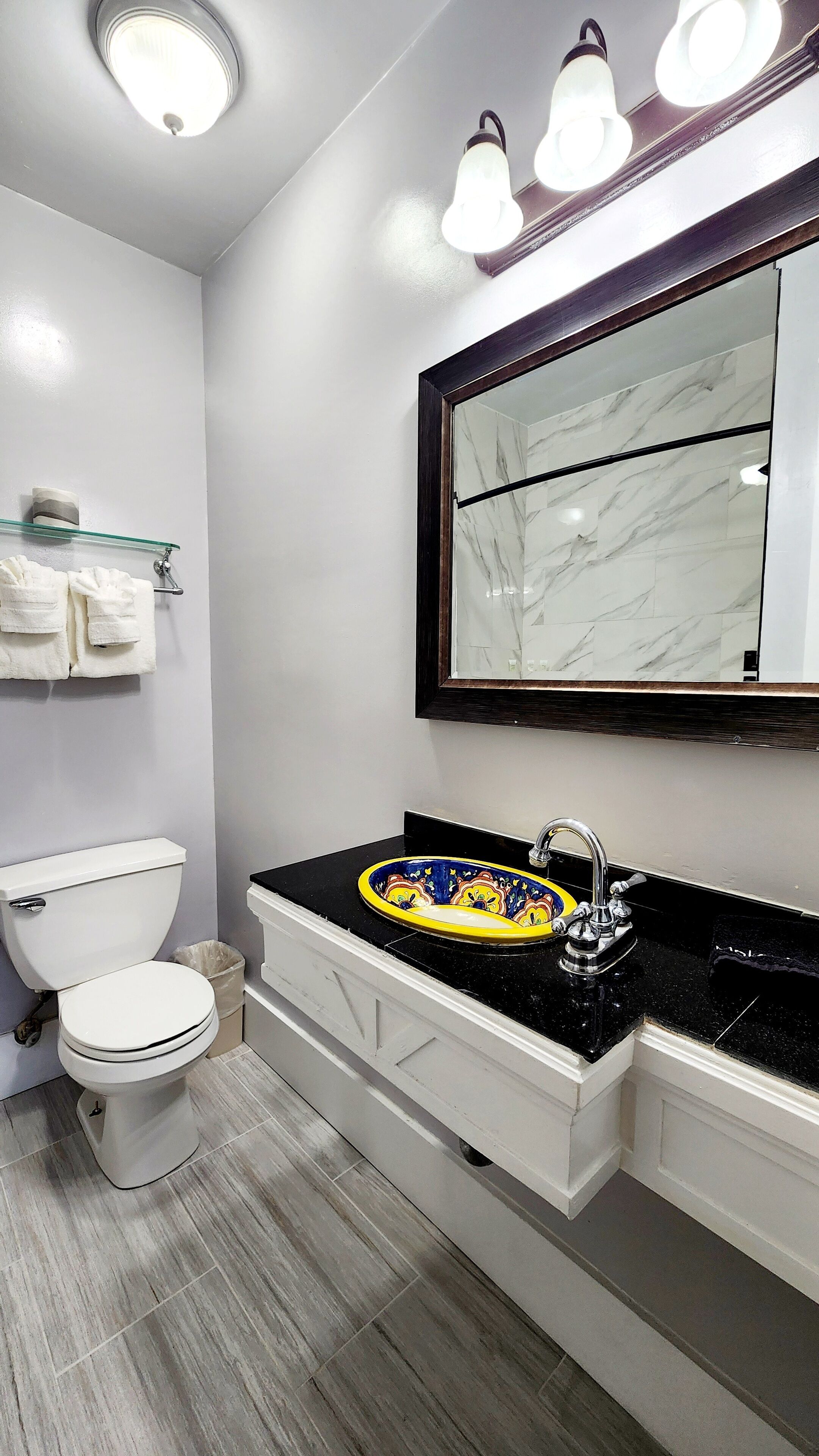 A modern bathroom with a toilet, a sink with a decorative basin, and a mirror with a marble frame.