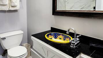 A modern bathroom with a toilet, a sink with a decorative basin, and a mirror with a marble frame.