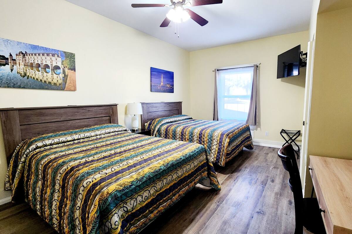 A hotel room with two beds, a ceiling fan, a TV, and a window with curtains.