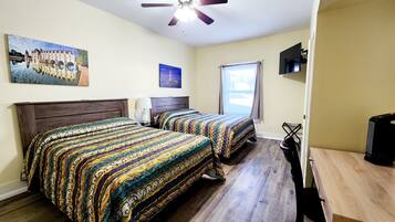 A hotel room with two beds, a ceiling fan, a TV, and a window with curtains.