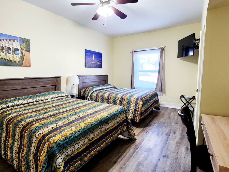 A hotel room with two beds, a ceiling fan, a TV, and a window with curtains.
