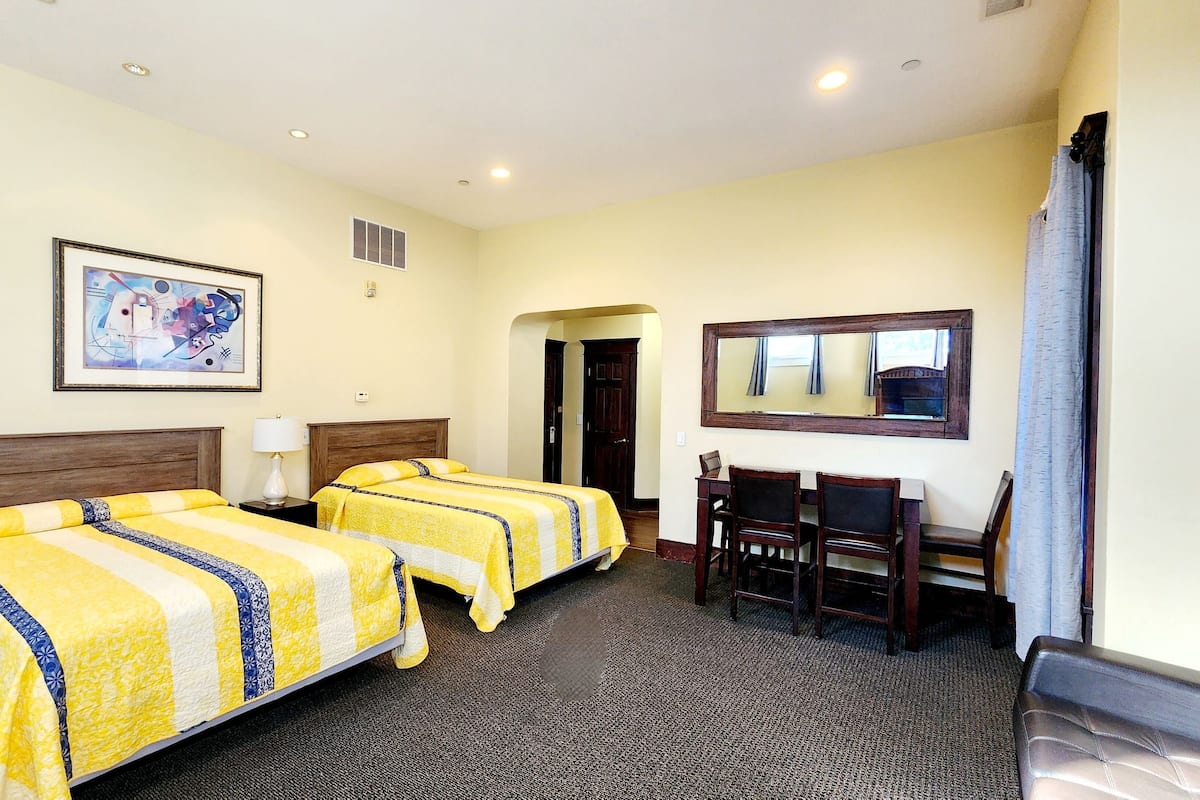 A hotel room with two beds, a dining table with chairs, a mirror, and a painting on the wall.
