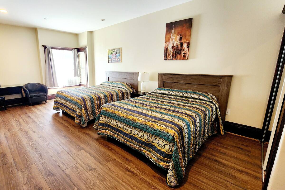 A hotel room with two beds, a desk, a chair, and a painting on the wall.