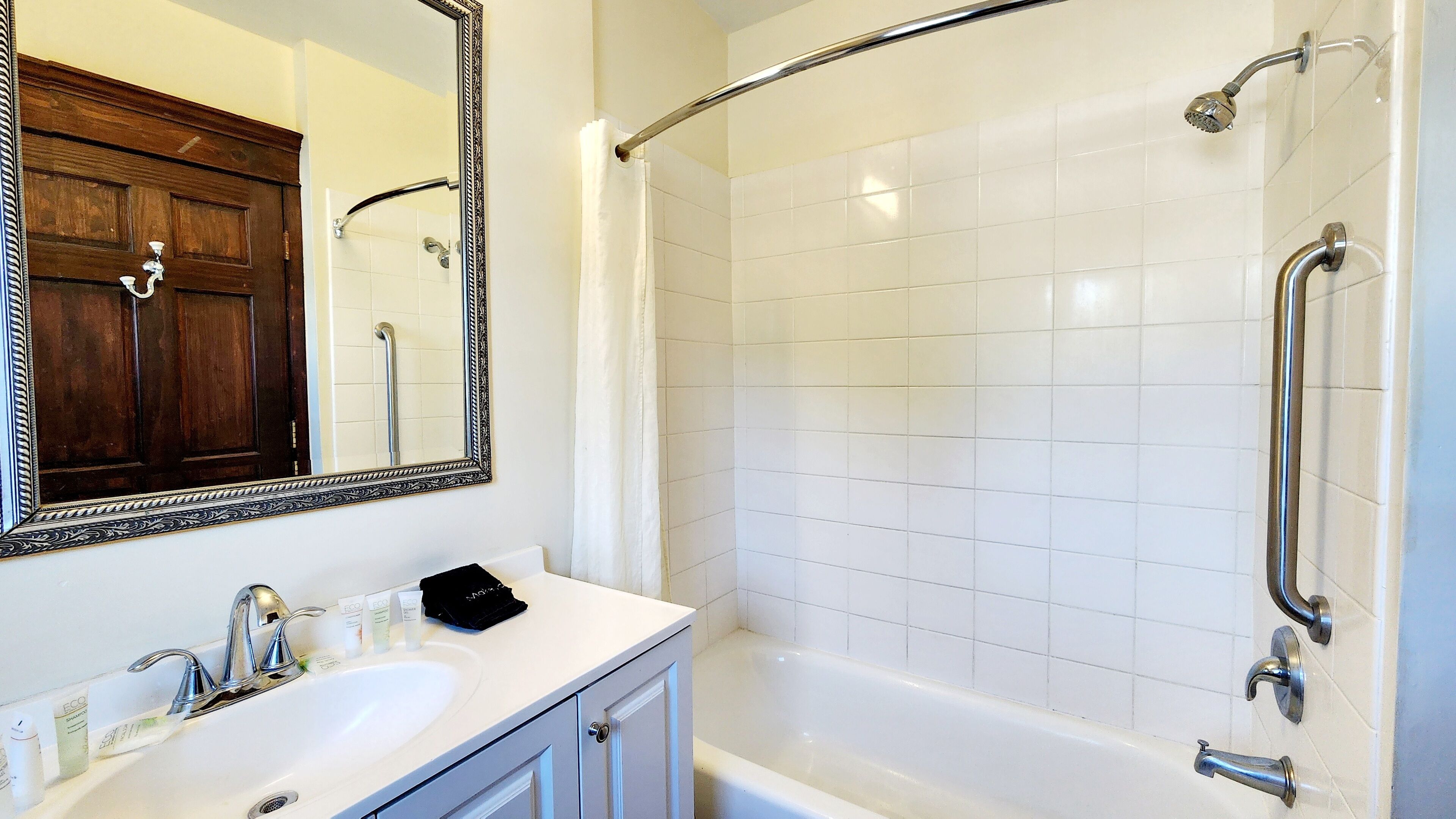 A bathroom with a white sink, vanity, and a walk-in shower with white tiles.