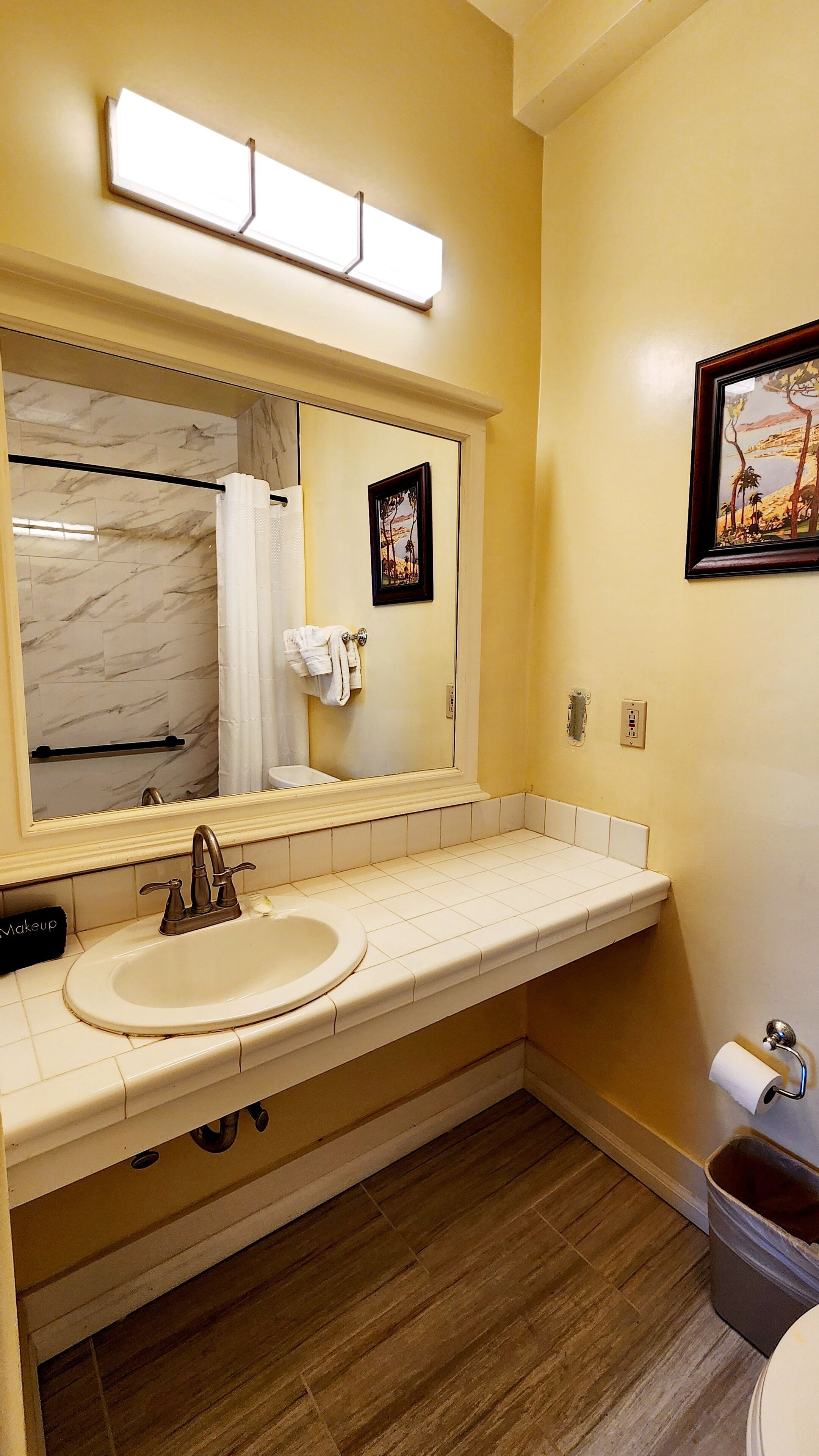 A bathroom with a marble-tiled shower, a sink with a vanity mirror, and a toilet.