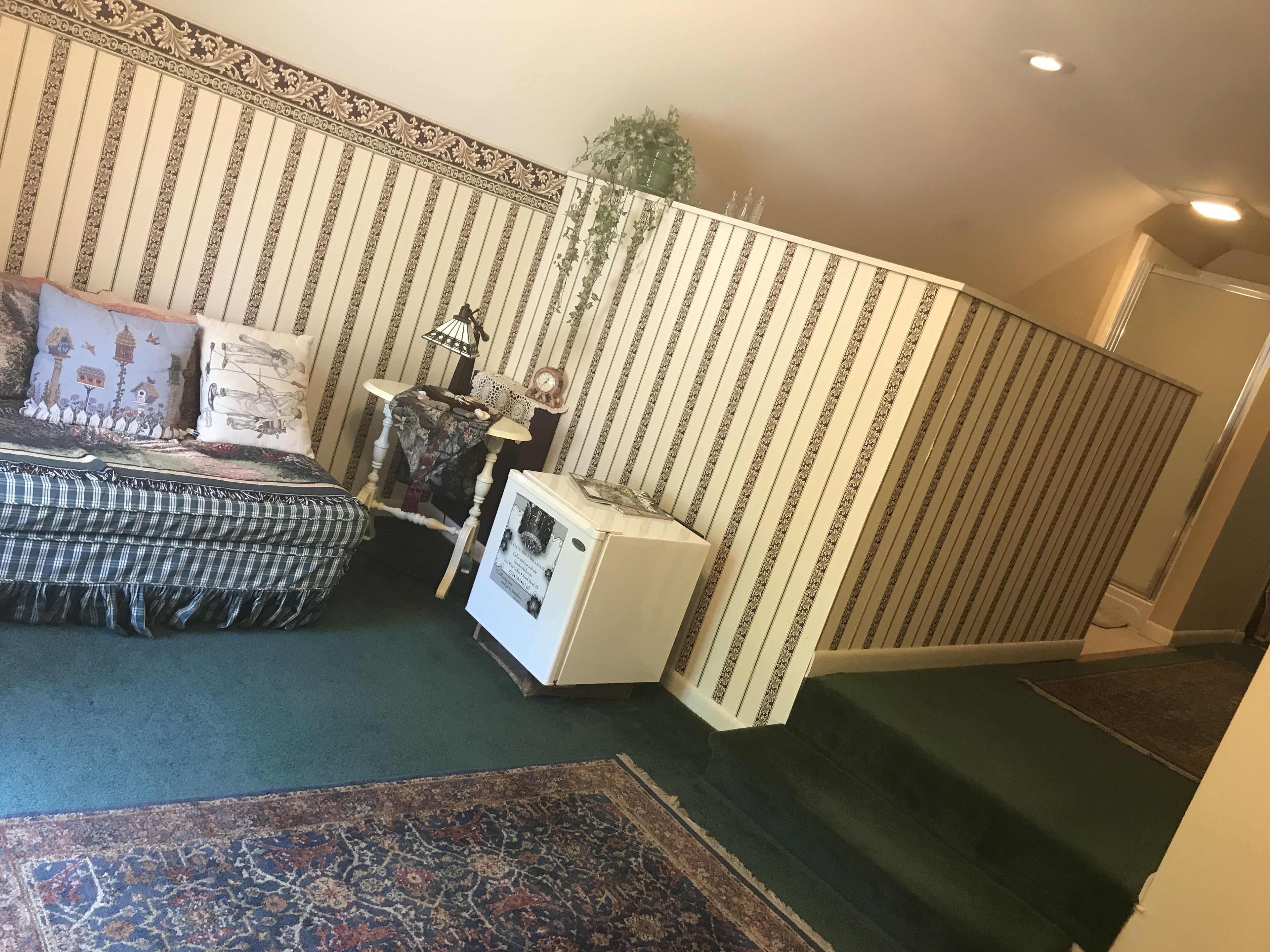 A bedroom with a bed, a small table with a lamp, a radiator, and a patterned wall.