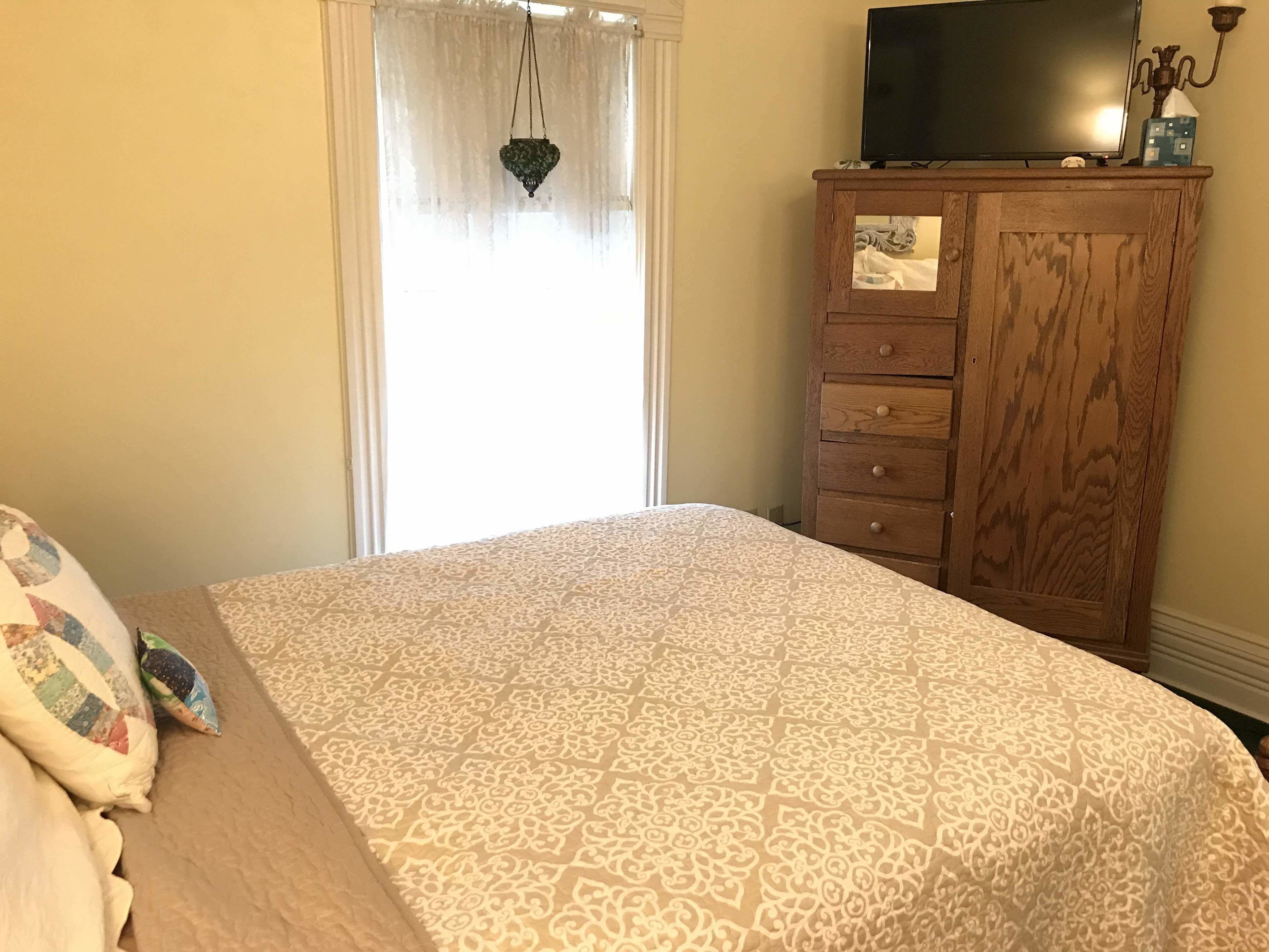 A bedroom with a bed, a dresser, a television, and a window with curtains.