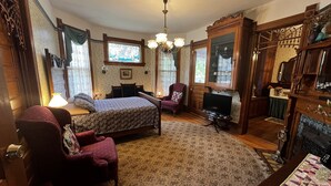 A traditional room with a bed, a television, a fireplace, and a large mirror.