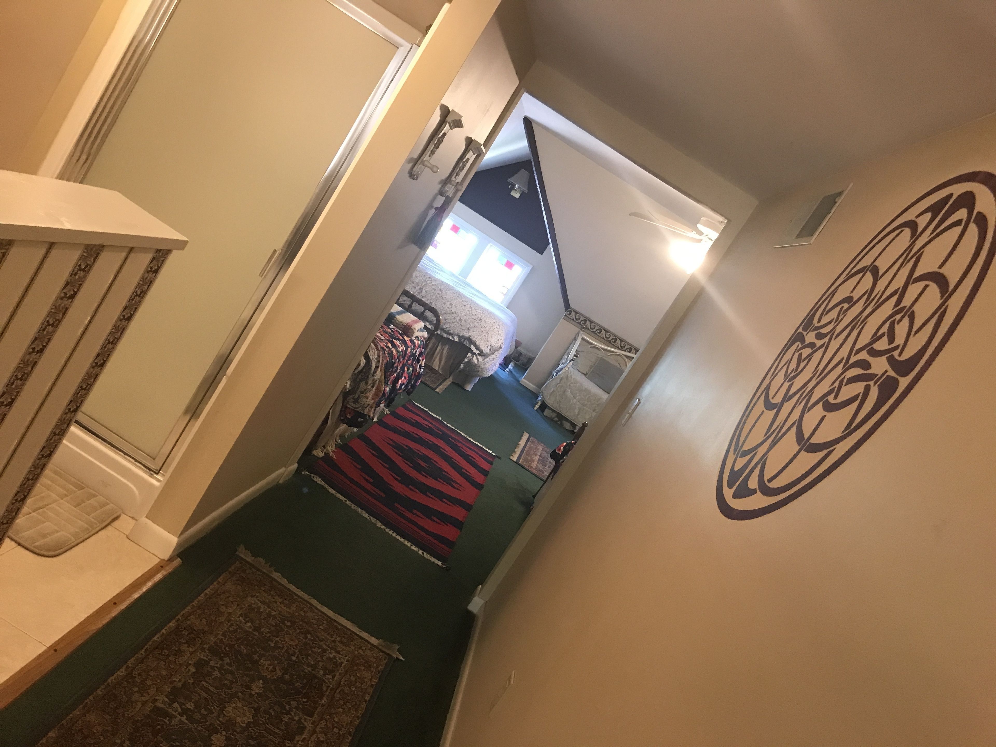 Ein Flur mit einem gemusterten Teppich, einem Bett mit Kopfteil und einer Wand mit einem runden Muster.