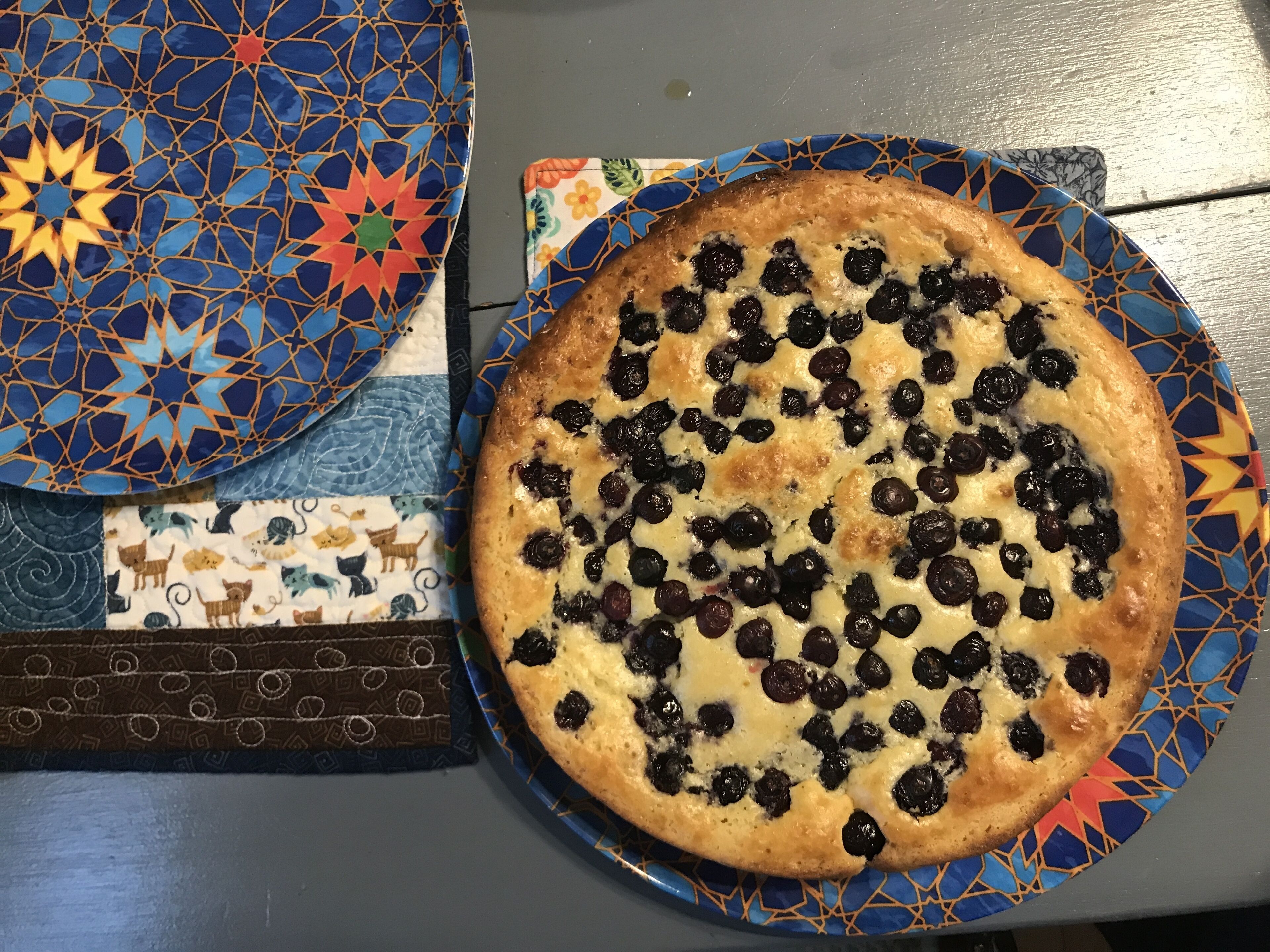 A round cake with blueberries on a blue patterned plate.