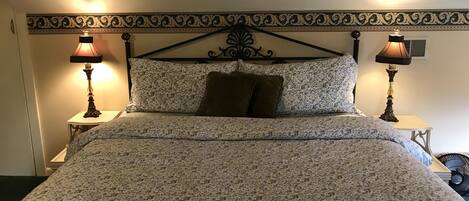 Uma cama com colcha estampada, duas luminárias de cabeceira e um painel decorativo de cabeceira.
