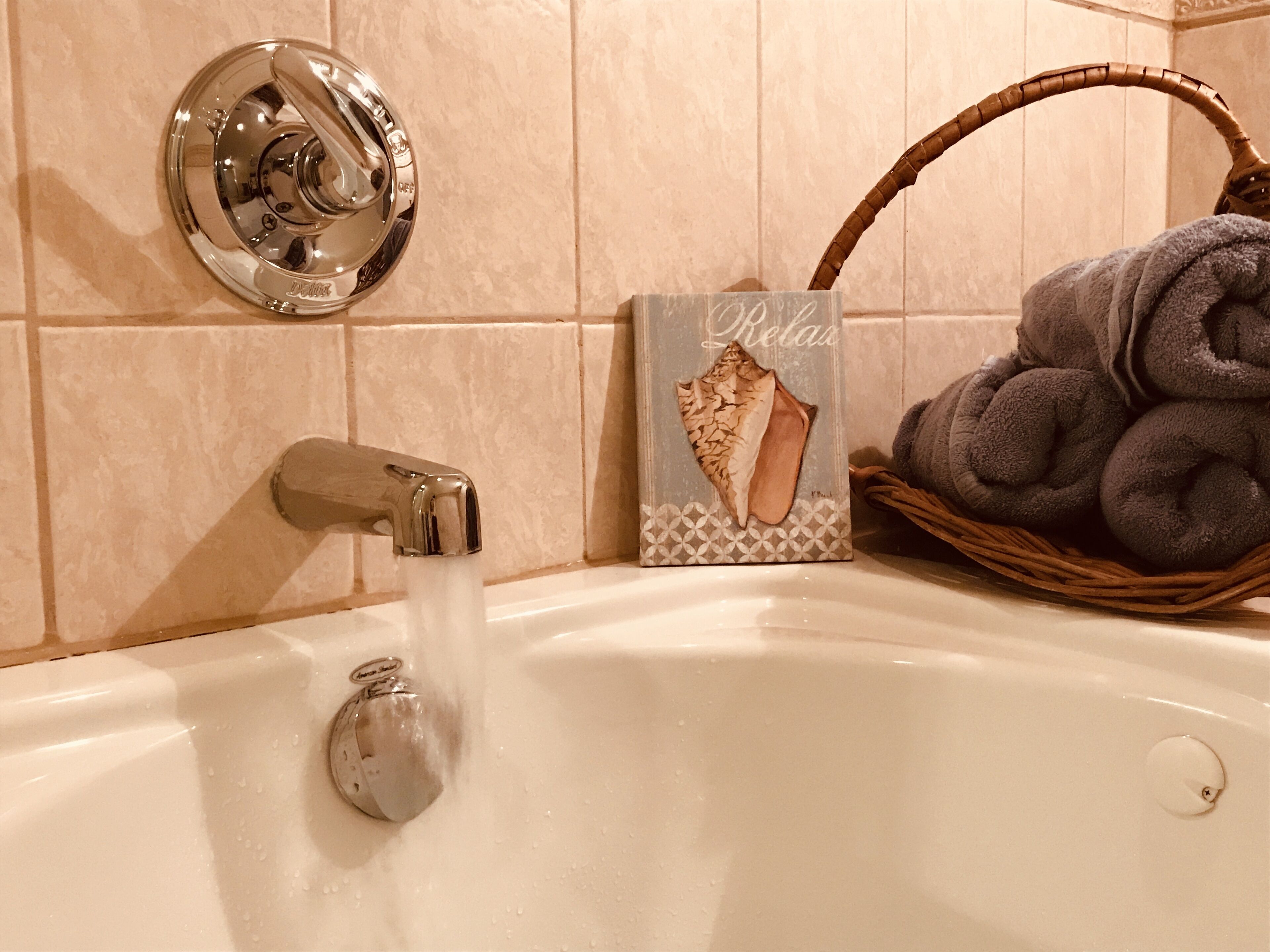 A bathtub with running water, a towel rack, and a decorative towel basket.