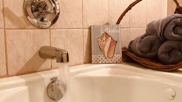 A bathtub with running water, a towel rack, and a decorative towel basket.