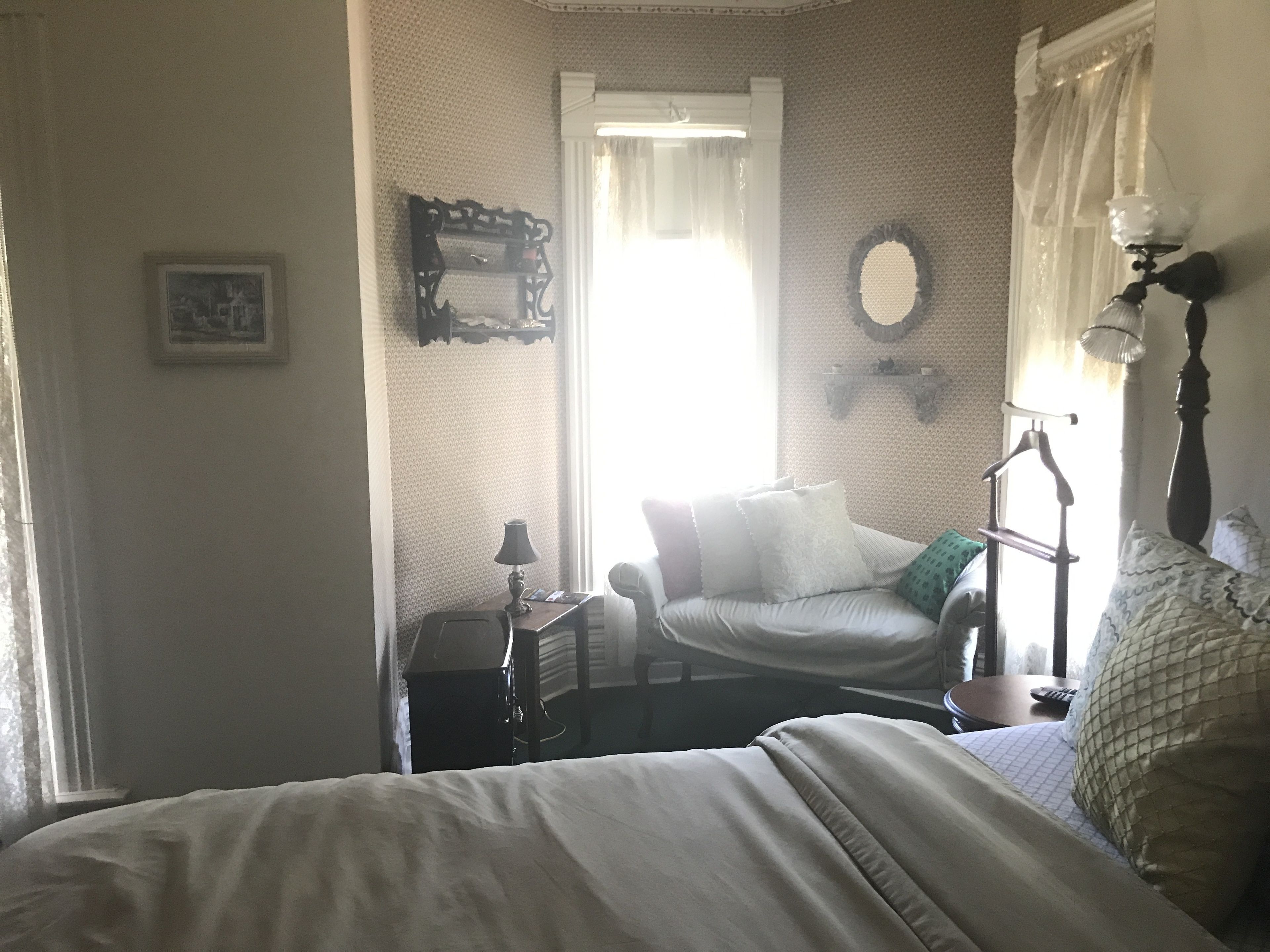 Un dormitorio con cama, una silla, una mesita de noche, una lámpara y un espejo.