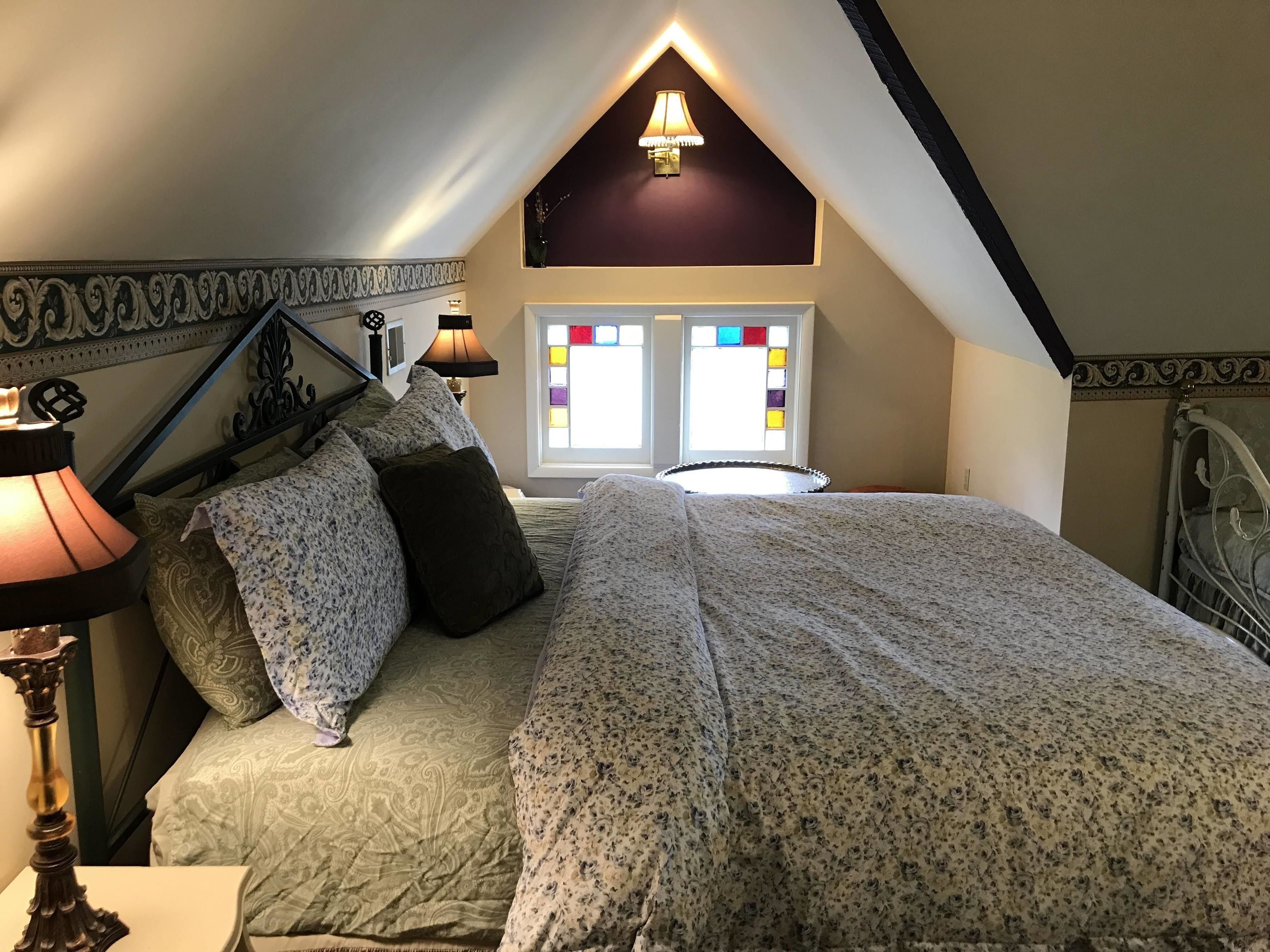 A bedroom with a bed, two bedside lamps, a window with stained glass, and a decorative wall.