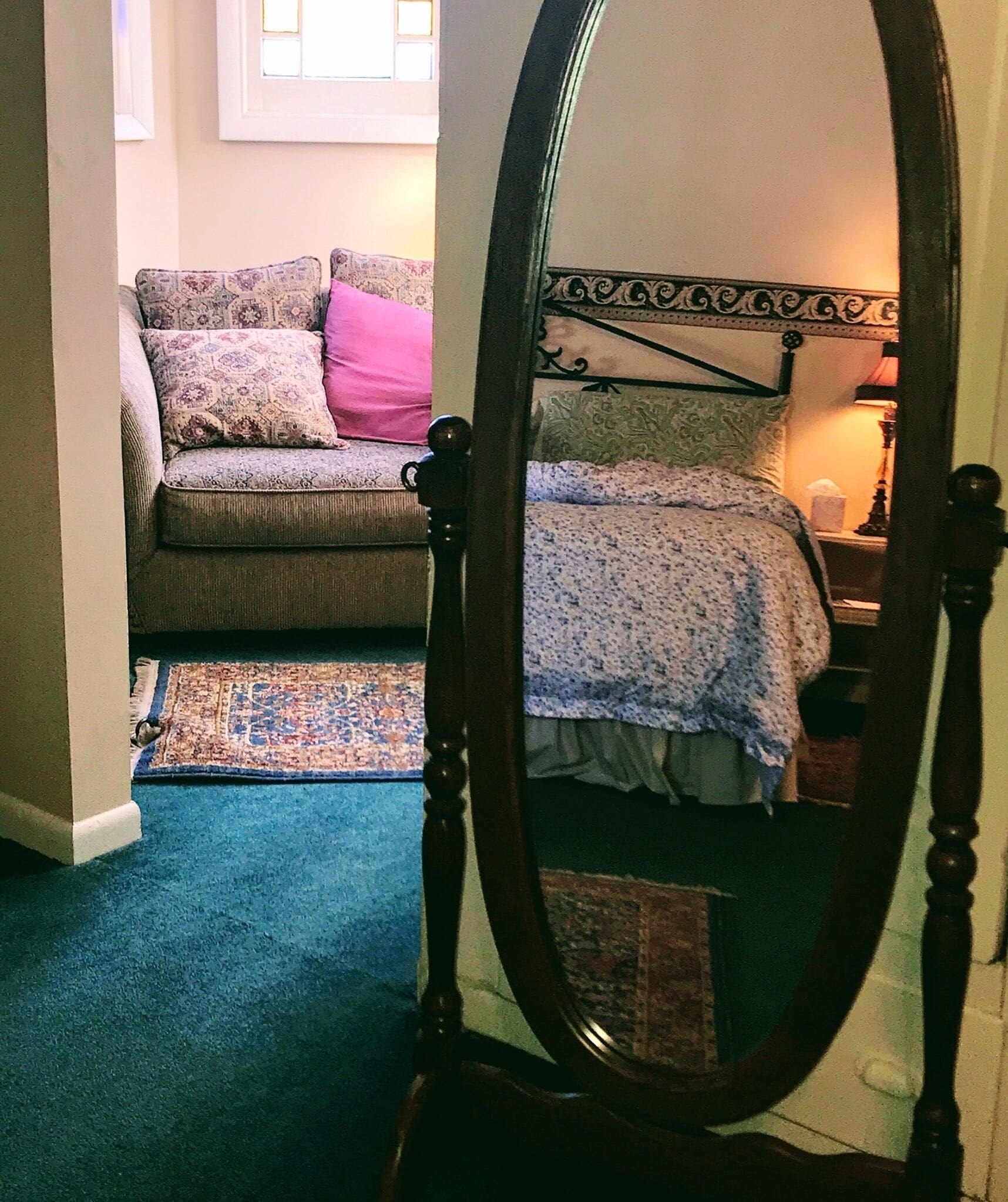 A bedroom with a bed, a nightstand, a lamp, a window, and a patterned rug.