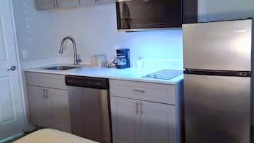 A compact kitchen with a dishwasher, a coffee maker, and a refrigerator.
