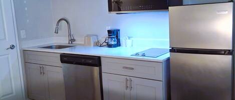 A compact kitchen with a dishwasher, a coffee maker, and a refrigerator.