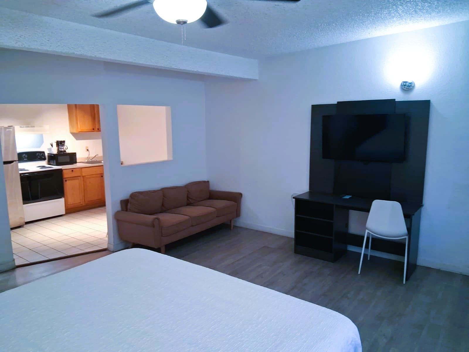 Une chambre avec un lit, une télévision, un bureau, une chaise et, au fond, une petite cuisine.