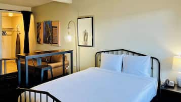 A hotel room with a bed, a desk, a chair, a lamp, and a phone on a bedside table.
