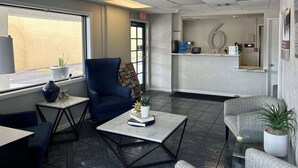 Un espace d’accueil comprenant un fauteuil bleu, une petite table avec un livre et une plante, ainsi qu’un comptoir de réception équipé d’un ordinateur et de brochures d’information.