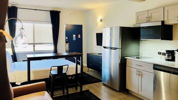 A compact hotel room with a bed, a small dining table, a refrigerator, a microwave, and a coffee maker.