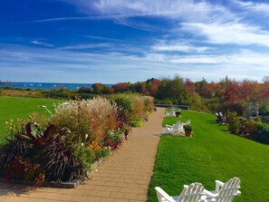 A pathway leading to a seating area with chairs, surrounded by well-maintained grass and plants, overlooking a body of water.