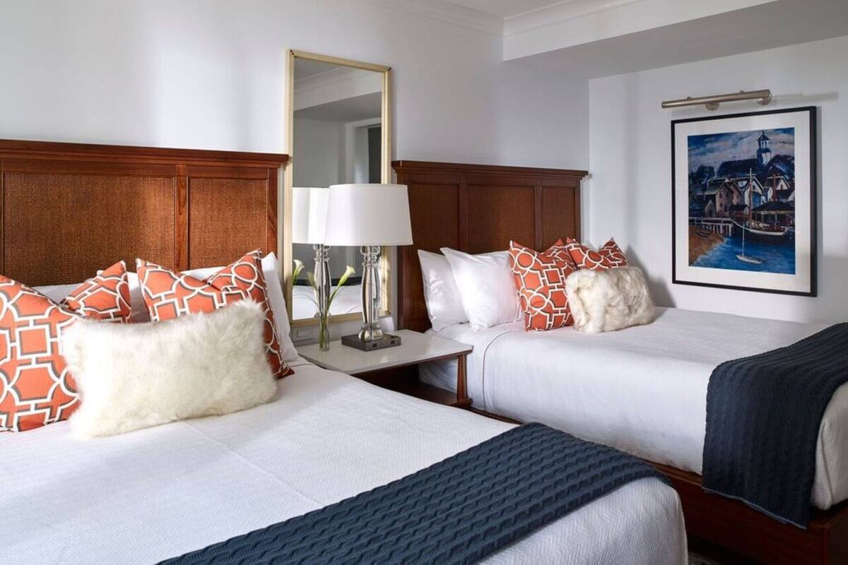A hotel room with two beds, a nightstand with a lamp, a mirror, and a framed picture on the wall.