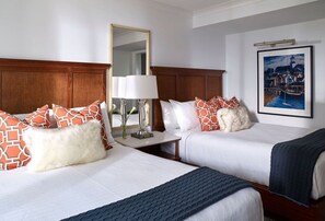 A hotel room with two beds, a nightstand with a lamp, a mirror, and a framed picture on the wall.
